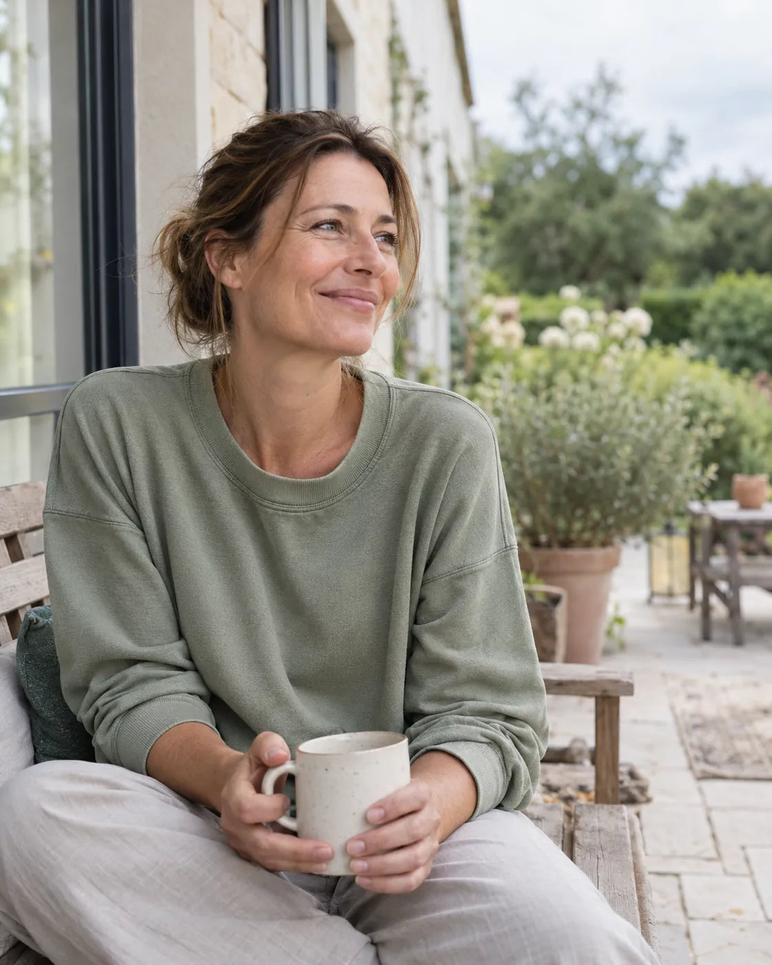 Frau mit einer Tasse in der Hand auf einer Gartenterrasse