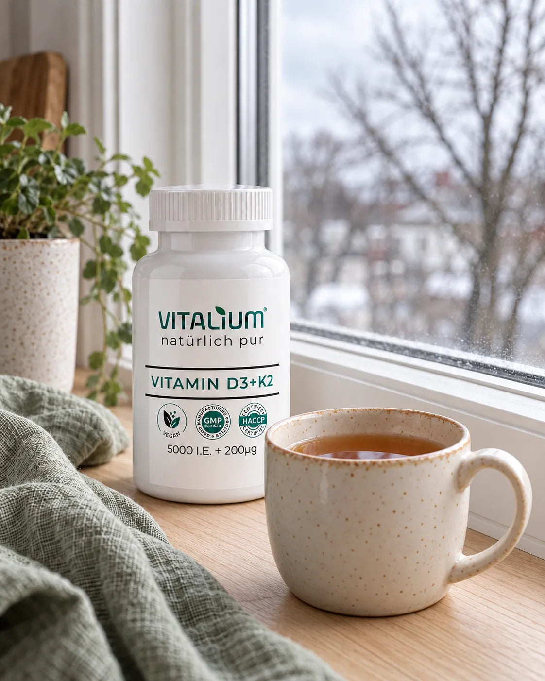 Vitamin D3 + K2 Dose und eine Tasse Tee auf der Fensterbank an einem Wintertag